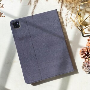 May include: A dark gray fabric iPad case with a camera lens cutout. The case is closed and the back is visible. The text "Book back." is visible in the top left corner of the image.
