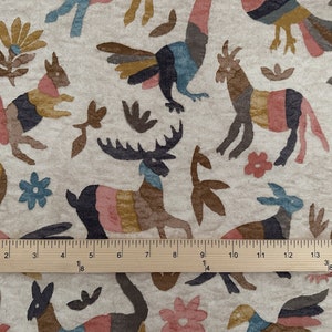 Puede incluir: Una tela beige con un patr&oacute;n repetido de animales y plantas estilizados en tonos de marr&oacute;n, rosa, azul y amarillo. La tela se mide con una regla de madera.