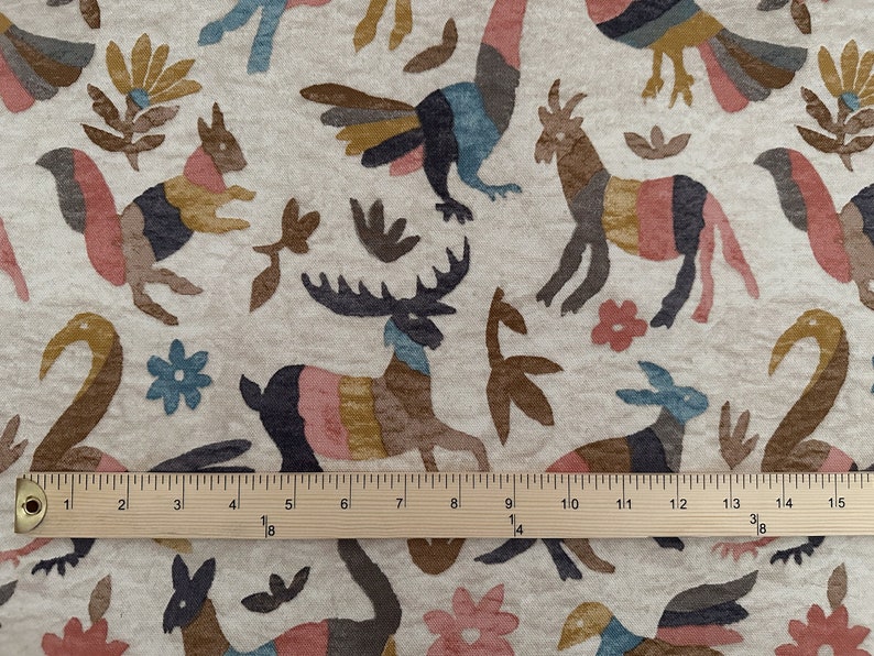 Puede incluir: Una tela beige con un patr&oacute;n repetido de animales y plantas estilizados en tonos de marr&oacute;n, rosa, azul y amarillo. La tela se mide con una regla de madera.