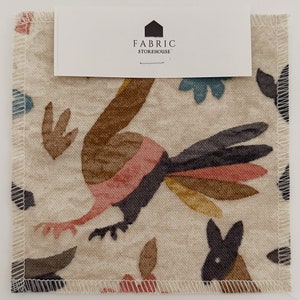 Puede incluir: Una muestra de tela con un fondo beige y un patr&oacute;n repetitivo de p&aacute;jaros y conejos estilizados en tonos de marr&oacute;n, rosa, azul y amarillo. El texto "FABRIC STOREHOUSE" est&aacute; impreso en una etiqueta blanca adherida a la muestra.