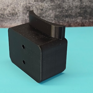 May include: A black 3D printed plastic mount with two holes and a curved top. The mount is designed to hold a device or object.