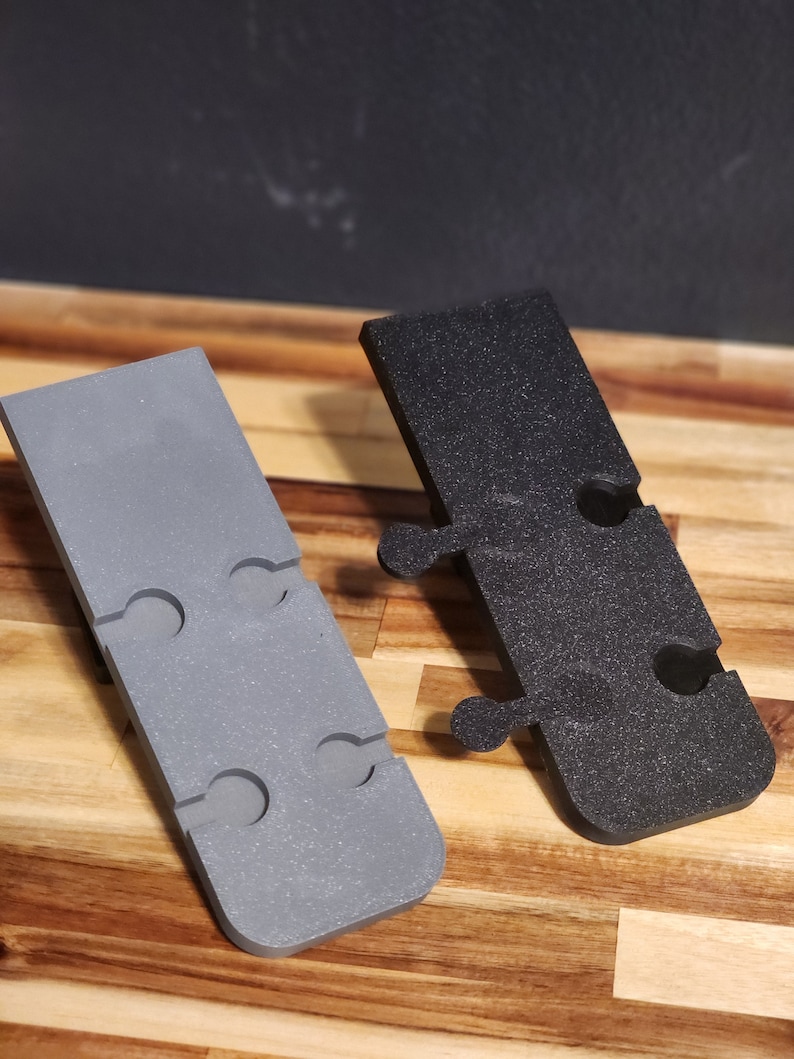 Puede incluir: Dos soportes de pared de pl&aacute;stico, uno gris y otro negro, con m&uacute;ltiples agujeros para colgar objetos. Los soportes est&aacute;n dise&ntilde;ados para ser fijados a una pared.