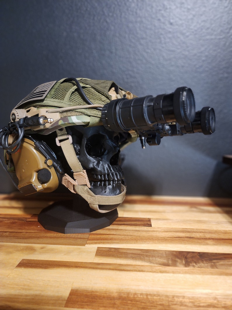 Pu&ograve; includere: Un casco tattico con visore notturno, montato su un supporto nero a forma di teschio. Il casco presenta tessuto mimetico, una toppa con la bandiera americana e protezioni per le orecchie color cachi. Il visore &egrave; nero.