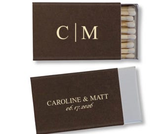 May include: Two brown matchboxes are displayed, one open and one closed. The closed box has the initials "C|M" in gold. The open box reveals matches and the text "CAROLINE & MATT 06.17.2026" in gold.