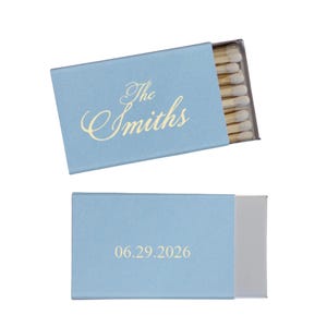May include: Two light blue matchboxes are displayed. One box is open, revealing matches. The top box has the text "The Smiths" in gold script. The bottom box has the date "06.29.2026" in gold.