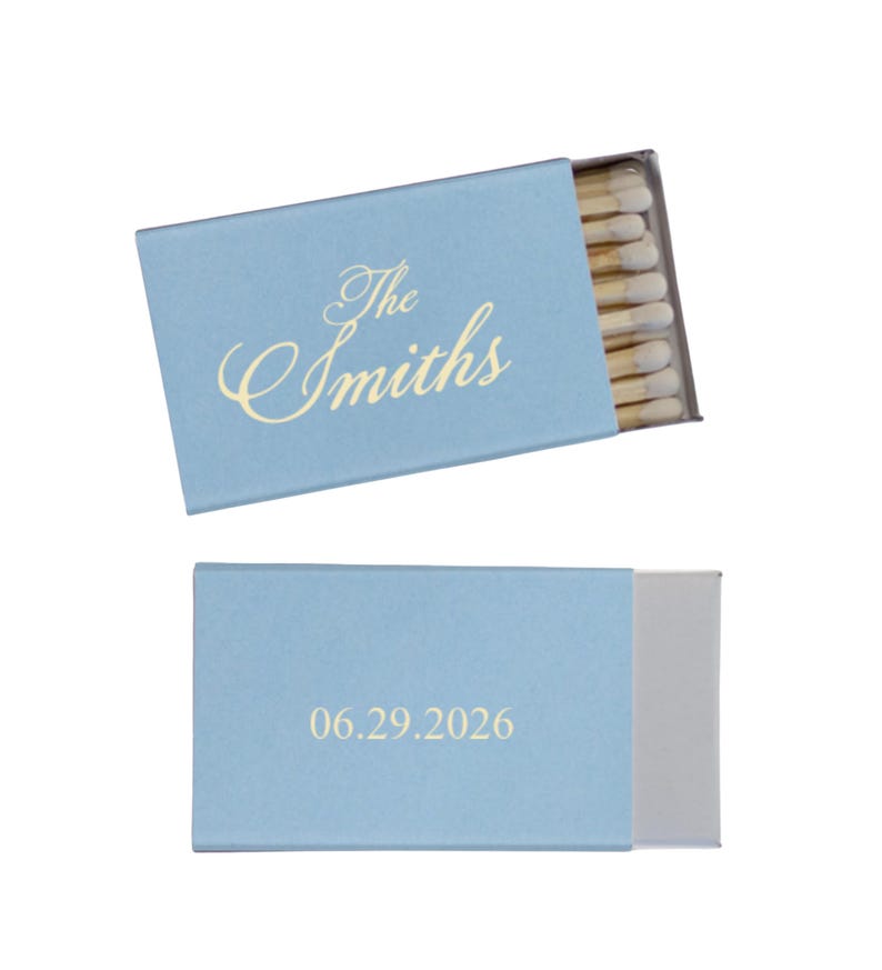 May include: Two light blue matchboxes are displayed. One box is open, revealing matches. The top box has the text "The Smiths" in gold script. The bottom box has the date "06.29.2026" in gold.