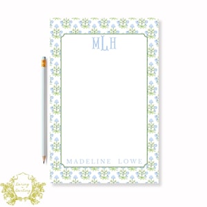 May include: A personalized notepad with a floral pattern in blue and green. The notepad features the initials "MLH" at the top and the name "Madeline Lowe" at the bottom. A light blue pencil rests on the left side.