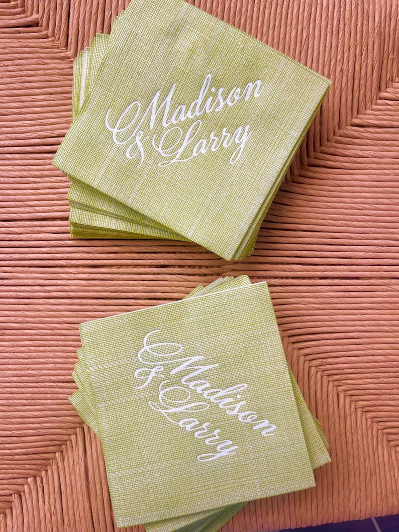 Pu&ograve; includere: Pile di tovaglioli quadrati verde chiaro con i nomi "Madison & Larry" in elegante scrittura bianca. I tovaglioli hanno un aspetto strutturato e sono disposti su una superficie intrecciata marrone chiaro. Ideale per un matrimonio o un evento speciale.