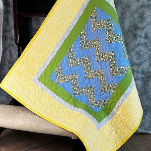 May include: A yellow, green, and blue baby quilt with a chevron pattern. The quilt has a white and yellow floral print border.