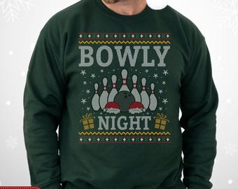 May include: Forest green sweatshirt with a festive bowling-themed design. The graphic includes bowling pins, a bowling ball, and the words "BOWLY NIGHT" in white. The design has a holiday sweater aesthetic, with snowflake accents.