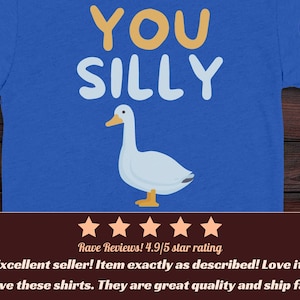 K&ouml;nnte beinhalten: Ein k&ouml;nigsblaues T-Shirt mit einer wei&szlig;en G&auml;nsegrafik, die &uuml;ber dem Text YOU SILLY in gelber und wei&szlig;er Schrift zentriert ist. Das Shirt enth&auml;lt ein kleines kreisf&ouml;rmiges True Royal-Etikett in der oberen rechten Ecke und das ZenFIT-Logo unten rechts.