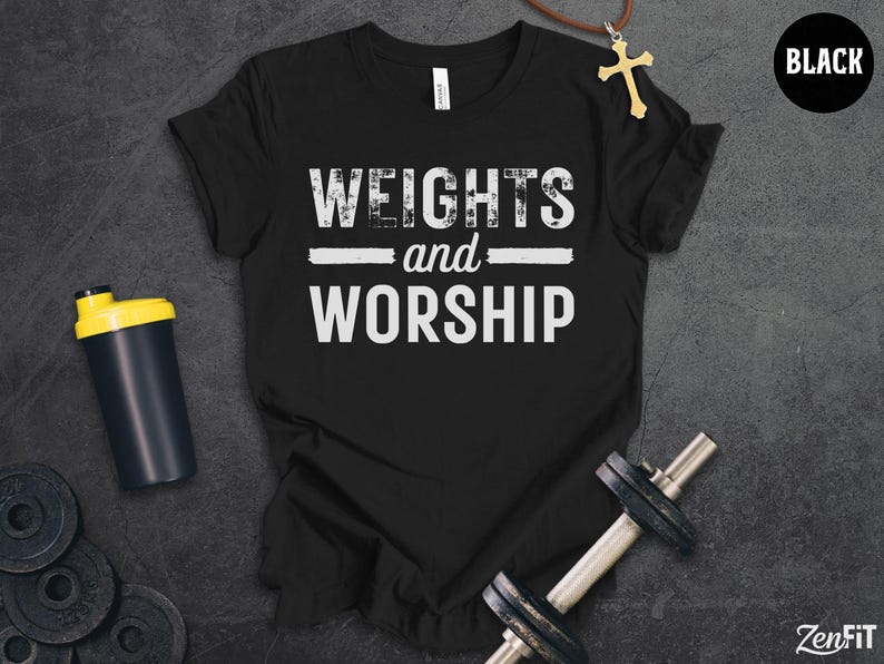 May include: A black t-shirt featuring the white distressed text "WEIGHTS and WORSHIP" centred on the chest. The shirt is accompanied by a black and yellow shaker bottle, a metal dumbbell, and a gold cross pendant on a brown cord necklace.
