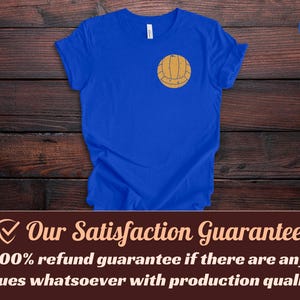 Puede incluir: Una camiseta de manga corta en color azul real con un peque&ntilde;o gr&aacute;fico centrado de un voleibol de color tostado con estilo vintage en la parte superior del pecho. La prenda tiene cuello redondo y un corte est&aacute;ndar con un dise&ntilde;o sencillo.