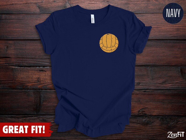 Puede incluir: Una camiseta de manga corta en color azul marino con un peque&ntilde;o gr&aacute;fico de un bal&oacute;n de voleibol amarillo desgastado situado en el pecho izquierdo. La prenda tiene cuello redondo y un corte est&aacute;ndar con un dise&ntilde;o sencillo de bal&oacute;n.