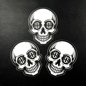 May include: Three black and white skull stickers with binary code in the eye sockets. The code reads "110 010 110 0 0 000".
