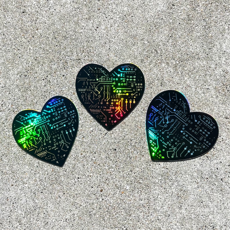 May include: Three iridescent black heart-shaped stickers with a circuit board design. The stickers have a rainbow holographic finish.