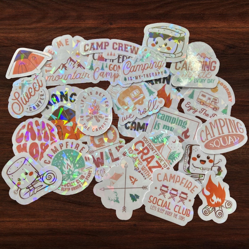 May include: A collection of holographic stickers with camping and outdoor themes. The stickers feature phrases like "Camp Crew", "Camping is my therapy", "Campfire Social Club", and "We roll Cami".