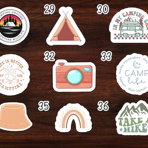 May include: Nine camping themed stickers with various designs. The stickers are white with rounded edges and feature illustrations of a campfire, a tent, a camera, a rainbow, a mountain range, a camper van, and a hat. The stickers also include text such as "Camping Ground", "Life is Better by the Campfire", "Camp Life", and "Take a Hike".