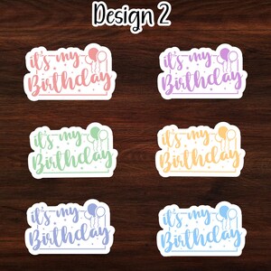 Puede incluir: Seis pegatinas coloridas con el texto "it's my Birthday" y globos. Las pegatinas est&aacute;n sobre un fondo de madera.