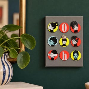 Könnte beinhalten: Eine graue rechteckige Tafel zeigt neun kreisförmige Magnete in einem Raster. Die Magnete zeigen Schwarz-Weiß-Porträts von Frauen mit verschiedenen Frisuren, farbige Hintergründe, die Buchstaben O und h sowie den Text admire en silence.