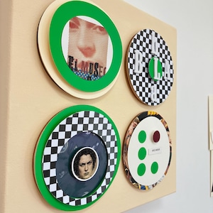 Könnte beinhalten: Eine quadratische beige Leinwand mit vier kreisförmigen Mixed-Media-Kunstwerken. Oben links ist ein Gesicht mit dem Text EL MUSEO zu sehen. Oben rechts befindet sich ein schwarz-weißes Schachbrettmuster mit den Buchstaben BLA. Unten links sind ein Gesicht und ein Schachbrettmuster zu sehen. Unten rechts befinden sich grüne Punkte und ein kleiner roter Kreis.