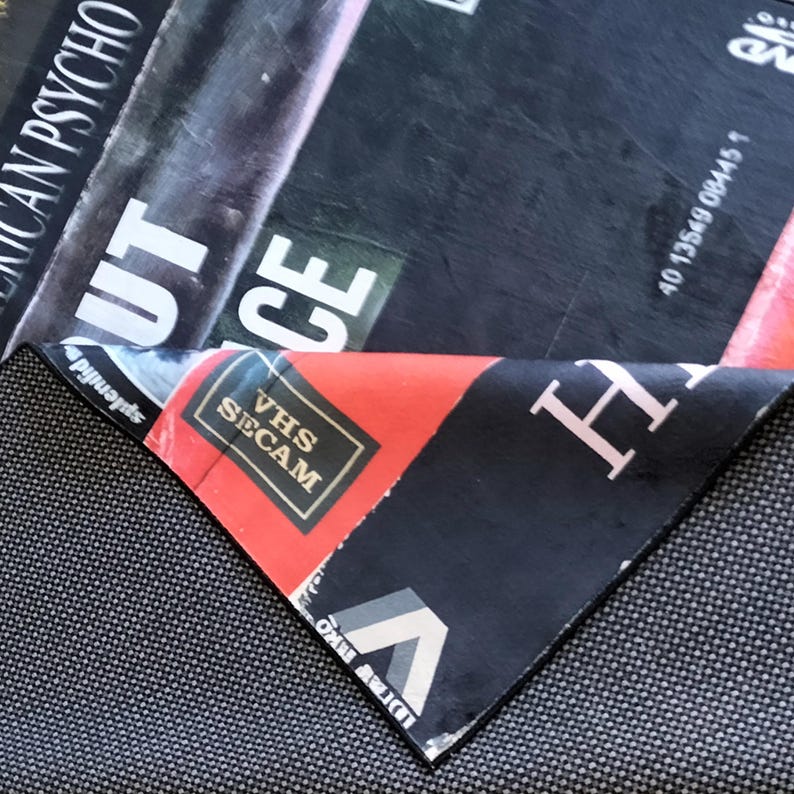 Może przedstawiać: Częściowo złożone etui na film z widocznym tytułem "American Psycho". Etui ma czarny i czerwony design z białymi literami. Widoczne jest r&oacute;wnież logo VHS SECAM.