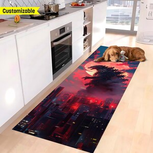 May include: A red and black kitchen rug with a Godzilla monster graphic and a red moon in the background. The rug is in a kitchen with white cabinets and a stainless steel oven.