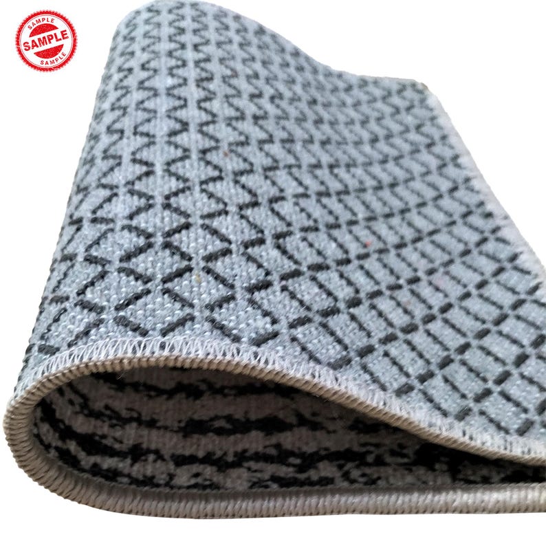 Puede incluir: Primer plano de una alfombra gris y negra con un borde blanco. La alfombra est&aacute; doblada por la mitad y el patr&oacute;n es visible en ambos lados.