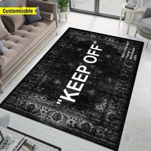 May include: A rectangular area rug featuring a distressed black and gray traditional pattern with the white text "KEEP OFF" printed in large capital letters across the center and additional text reading "IKEA c/o Virgil Abloh "Flooring" Almhult, Sweden c.2019" in the corner.