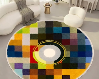 Könnte beinhalten: Ein runder, bunter Teppich mit einem geometrischen Muster aus Quadraten in den Farben Gelb, Blau, Grün, Rot und Lila. Die Mitte des Teppichs zeigt ein konzentrisches Kreisdesign mit einem weißen Zentrum.