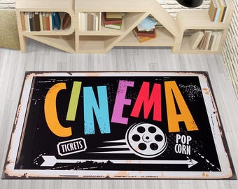 May include: A black and white vintage-style rug with the word "CINEMA" in colourful letters. The rug also features a film reel, the words "TICKETS" and "POP CORN", and arrows pointing in opposite directions.
