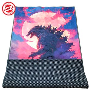 May include: A black and grey Godzilla rug with a pink and blue background. The rug features a large, full moon with Godzilla standing in front of it. The rug has a black and grey checkered border.