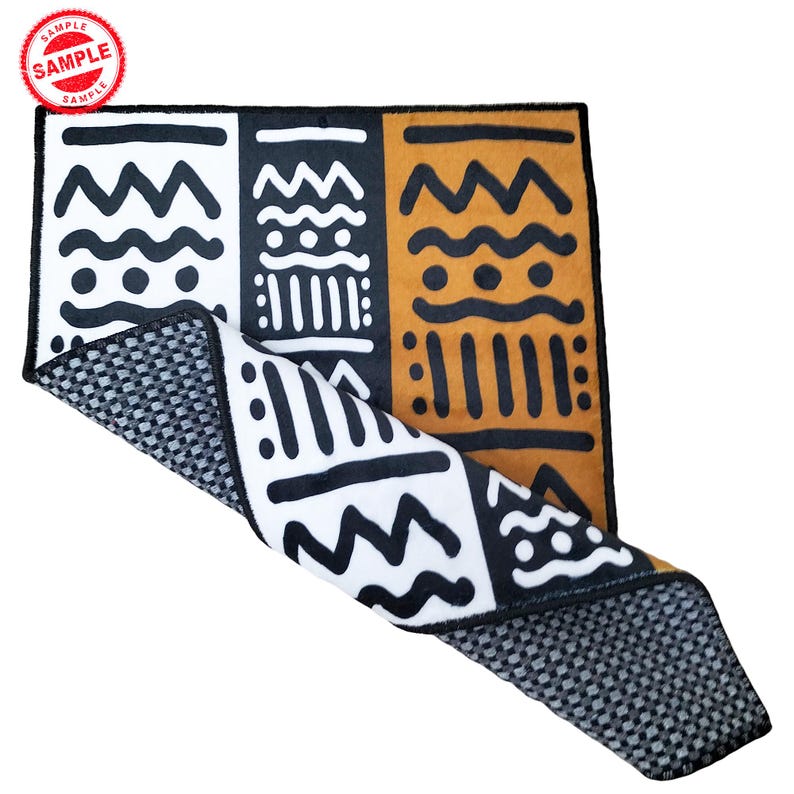 May include: A black, white, and orange patterned bath mat with a black and gray textured backing. The mat is folded in half and the patterned side is facing up.