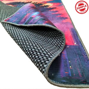 May include: A close-up of the back side of a rug with a gray checkered pattern. The rug has a colorful design on the front side, featuring a cityscape with a sunset in the background. The rug has a gray border.