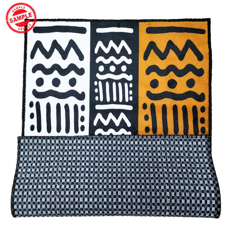 May include: A black, white, and orange patterned rug with a black and white checkered backing. The rug features geometric shapes and designs.