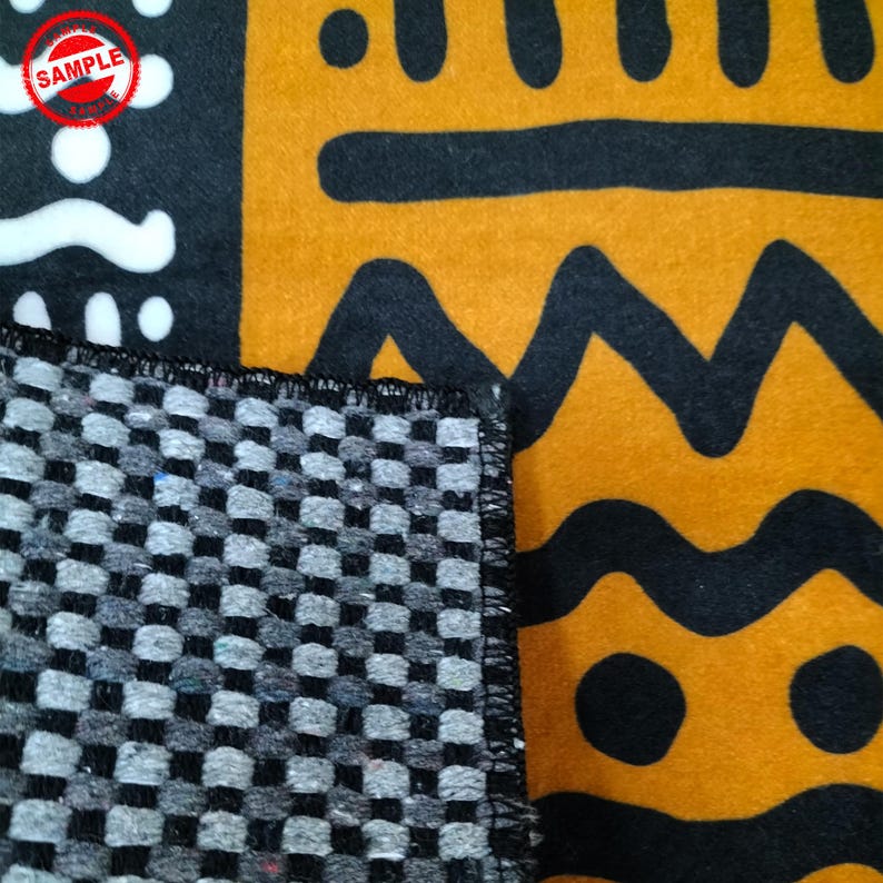 May include: Close-up of the back side of a black and white patterned rug. The back side is a black and white checkered pattern. The front side of the rug is visible in the background and features a yellow, black, and white geometric pattern.