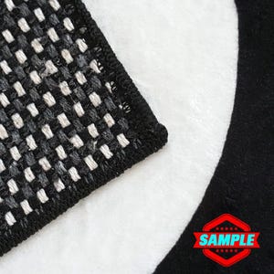 May include: Close-up of a black and white checkered rug with a black border. The rug is folded in half and the edge is visible. The rug has a white background with black squares.