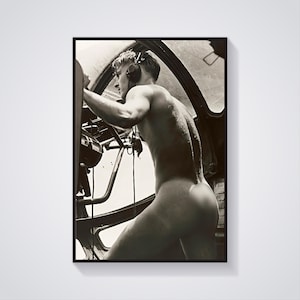 Puede incluir: Una fotografía en blanco y negro de un hombre en una cabina de mando, con auriculares y mirando hacia la izquierda. Está desnudo de cintura para arriba.