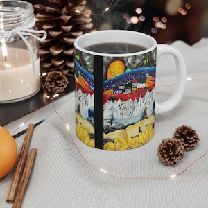 May include: White ceramic coffee mug with a colorful, abstract design featuring mountains, a sun, and the words "Lock Video" and "Poor Home." The design is reminiscent of a painting.