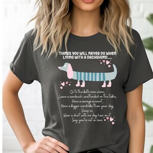 May include: A gray t-shirt with a cartoon dachshund and the text "Things you will never do when living with a dachshund..."  The text lists things like "Go to the bathroom alone", "Leave a sandwich unattended on the table", "Have a savings account", "Have a bigger wardrobe than your dog", "Sleep in", "Wear a shirt with no dog hair on it", and "Say you're not in love".
