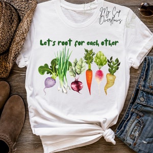 May include: White t-shirt with the text "Let's root for each other" and a row of colorful vegetables, including a carrot, onion, radish, turnip, and beet.