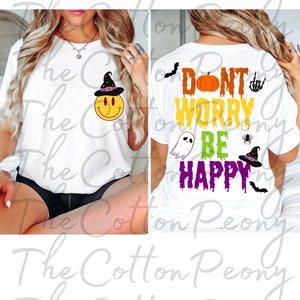 May include: White t-shirt with a Halloween-themed design. The front features a yellow smiley face wearing a witch hat. The back displays the phrase "Don't Worry, Be Happy" with Halloween graphics.