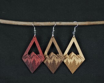 Könnte beinhalten: Drei Paar Holzohrringe mit einem Bergmotiv. Die Ohrringe sind diamantförmig und haben einen Ausschnitt in der Mitte. Die Ohrringe sind in drei verschiedenen Holztönen erhältlich: Rot, Braun und Natur.