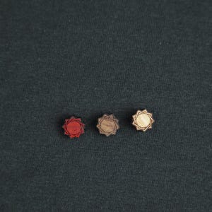May include: Three wooden decorative buttons with a starburst design. The buttons are red, brown, and natural wood.
