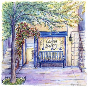 May include: A watercolor painting of a bakery storefront with a blue awning and the words "Levain Bakery" in white lettering. A blue bench sits in front of the storefront, and a tree with red flowers hangs over the entrance.