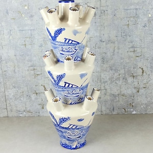 May include: A white ceramic vase with blue and white floral designs. The vase is made up of three stacked sections, each with a unique design. The vase has multiple openings for flowers.