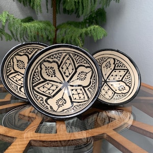 May include: Three white ceramic bowls with black geometric designs. The bowls are stacked on top of each other and have a glossy finish.