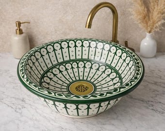 May include: A decorative ceramic sink with a green and white floral pattern. The sink has a gold-colored drain and is set against a neutral background. A gold faucet and soap dispenser are visible.