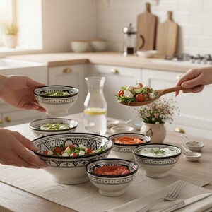 Peut inclure: Ensemble de bols en céramique blanche avec motifs géométriques noirs, remplis de salades et de sauces. Les bols sont disposés sur une table en bois avec une nappe neutre, avec des couverts et une carafe d'eau. Une cuillère en bois contient une salade.