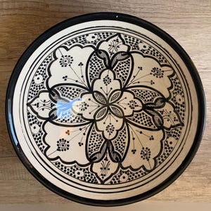 May include: A white ceramic bowl with a black rim and intricate black floral design.